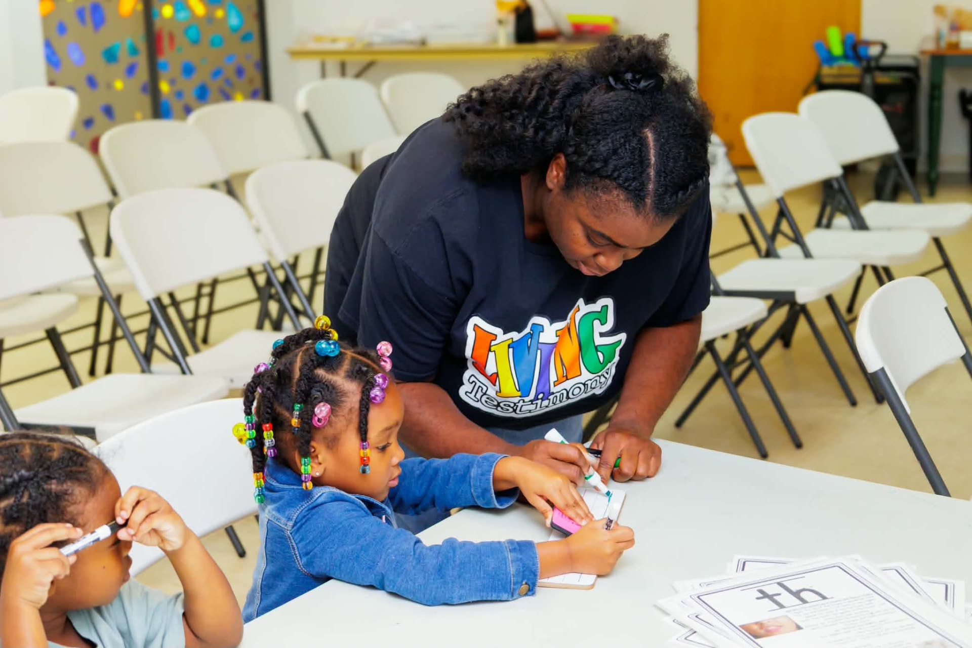 Coach guiding two students through letter practice with flash cards